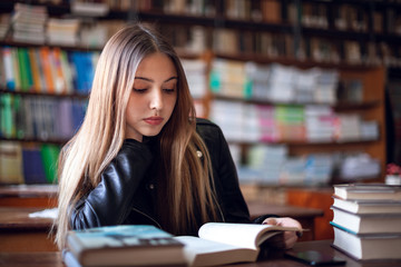 Beautiful teenager schoolgirl sitting in the library and reading a book