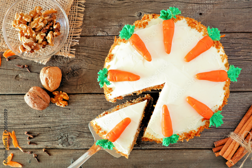 Poster Homemade carrot cake with cream cheese frosting. Top view table scene  with slice being removed. Close up over a rustic wood background.