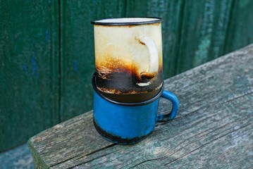 two old charred metal mugs on a gray wooden table against a green wall