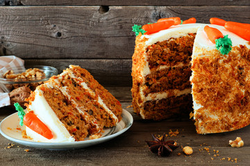 Slice of homemade carrot cake with cream cheese frosting and fondant carrots. Side view table scene with a dark wood background.