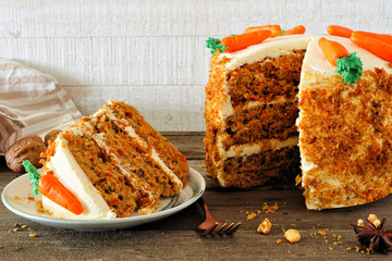 Slice of homemade carrot cake with cream cheese frosting and fondant carrots. Side view table scene...