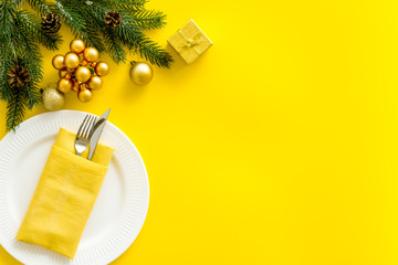 Table setting with spruce, plate, flatware on yellow background top view mockup