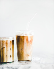 Homemade iced latte coffee in glasses on marble table, white background, copy space. Summer cold refreshing drink concept