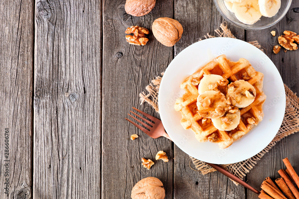Poster breakfast waffle with bananas, walnuts and syrup. top view side border with copy space over a wood b