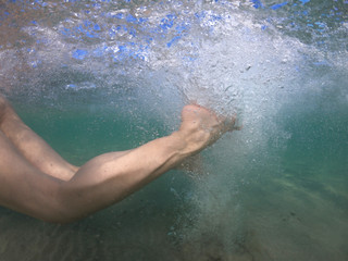 Obraz na płótnie Canvas Unidentified woman's feet underwater swimming with effort and releasing air bubbles to reach the shore