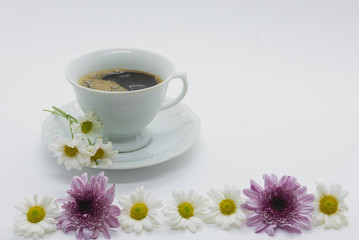 cup of coffee on table with colorful daisies on white background.