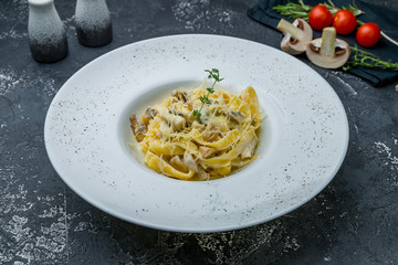 fettuccine with porcini mushrooms on white plate on dark grey concrete table