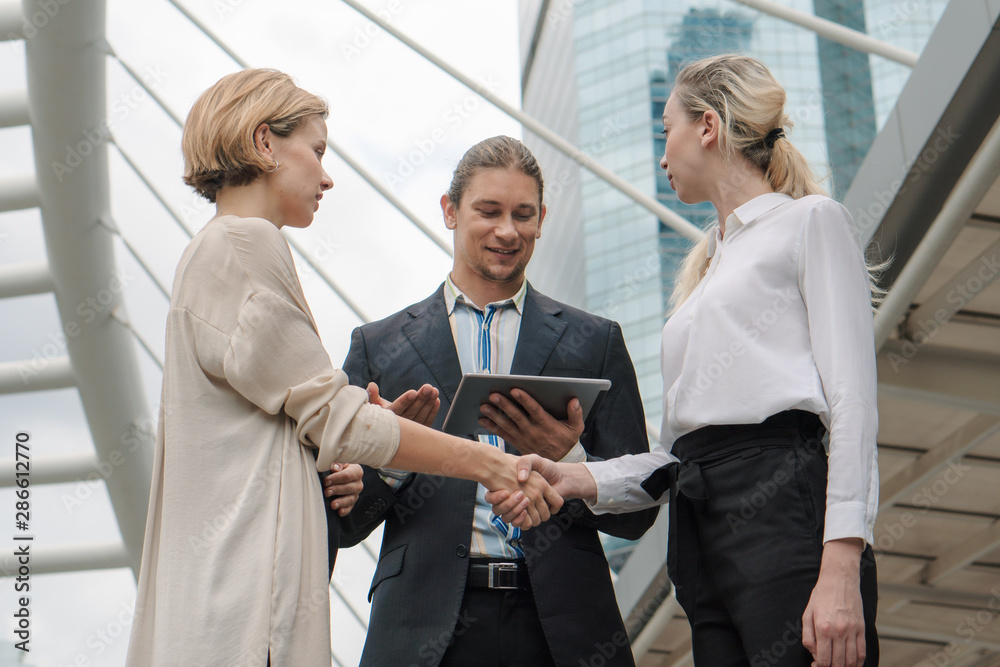 Wall mural two caucasian business woman having handshake to have greeting with caucasian businessman standing with tablet on hand