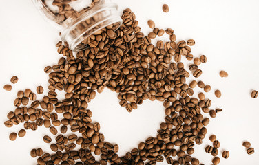 Coffee beans on a white table from a glass jar in the form of a heart