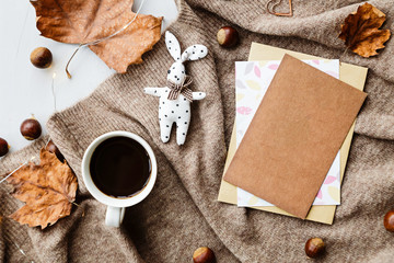 Autumn composition. Cup of coffee, blanket, autumn leaves, paper on brown background