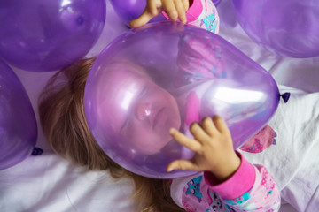 Naklejka premium Cute little girl in stylish dress celebrating birthday day with purple balloons