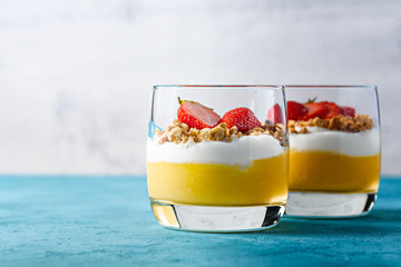 mango mousse with granola, ricotta and strawberries on white blue background