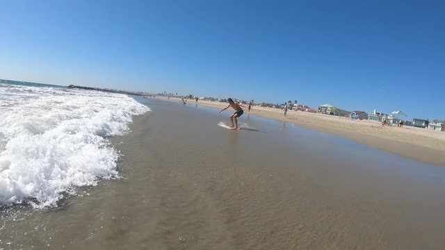 Young man riding skim board on the beach into the waves on the California Coast.