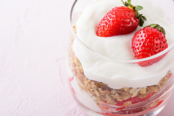 close up dessert with whipped cream, granola and strawberries on pink background