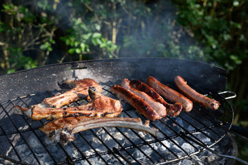 Quatre saucisses et trois de cotes d'agneaux sur un barbecue dans un jardin vues de face