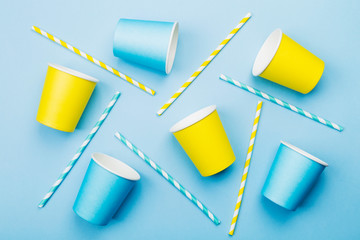 Blue and yellow paper cups and straw on yellow background. Top view
