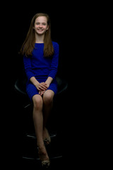 Fototapeta premium Charming girl teenager sitting on a chair in the studio on a bla