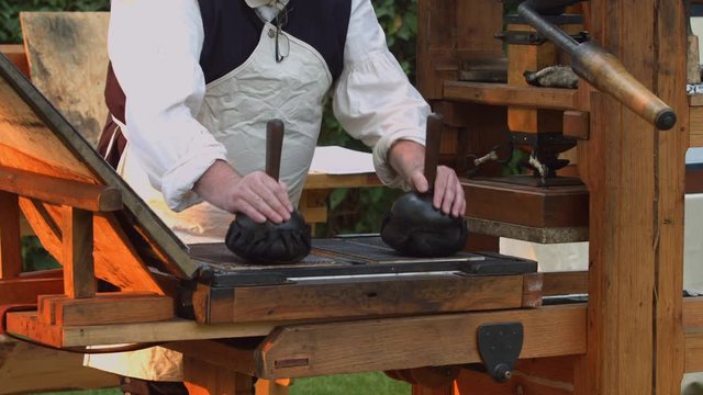 A revolutionary war re-enactor applies ink to the metal plates of an old 1700s printing press.