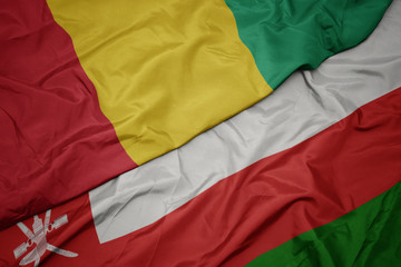 waving colorful flag of oman and national flag of guinea.