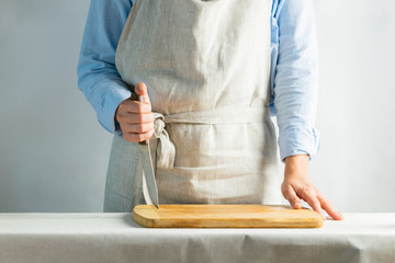 Woman cook in a cotton apron holds a cutting board and a knife in her hands. Rustic natural style. Kinfolk concept.