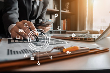 Male businessman or Designer using smartphone  with laptop and document on desk in modern office with virtual interface graphic icons network diagram.