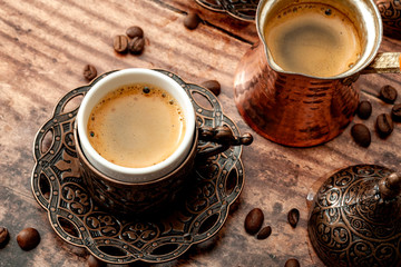 Traditional digestive drinks and serve a strong shot of espresso to stay awake conceptual idea with copper coffee pot, metal cup with ethnic embossed ornament and roasted beans on wooden backgrounds