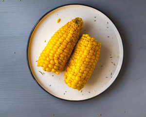 Boiled corn on a ceramic plate, two halves, shot at close range