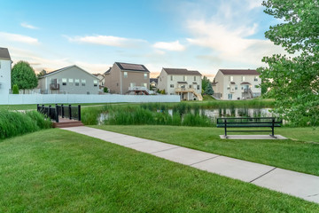 Neighborhood park with pond bridge pathway bench and trees in front of homes