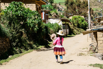 girl and baby, wearing traditional Andean dress and hat, walking in a street in the Peruvian highlands.
