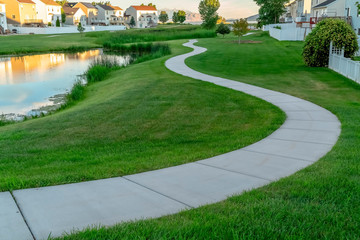 Winding footpath along a shiny pond in front of homes viewed on a sunny day