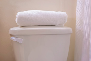 Close up of the tank of a toilet with a folded white towel on top of the lid