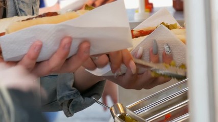 Girls' hands put various seasonings on a hot dog in a special kiosk of street food, fast food on the Amsterdam street.