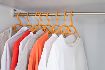 Coral and White colour clothes on hangers in wardrobe in dressing room. Several blouses and shirts for casual outfit. Fashion  background with copy space.
