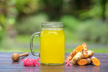 Energy tonic drink with turmeric, ginger, lemon and honey in glass mug, nature background, close up