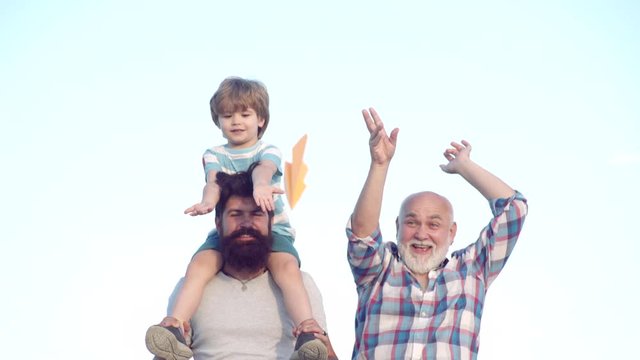 Multi generation. Family generation: future dream and people concept. Happy grandfather father and grandson with toy paper airplane over blue sky and clouds background.