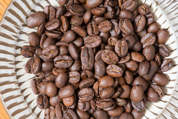 Coffee beans on a plate placed on a wooden table.
