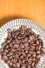 Coffee beans on a plate placed on a wooden table.