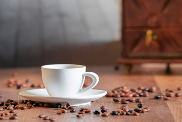 Photo detail of many coffee beans surrounding a white porcelain cup with selective focus on a wooden table. Concept of relaxation and aroma of coffee.