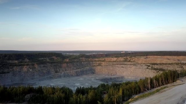 huge grey gravel mining quarry against small town silhouette at dense forest in summer upper view. Concept ecosystem disturbance