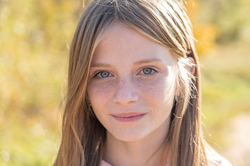 Fototapeta premium Beautiful blonde young girl with freckles outdoors on nature background in autumn, close up portrait