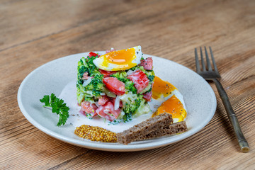 Delicious salad with broccoli, tomato, onion and boiled egg with cream sauce in plate on wooden background. Healthy food