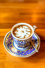 A cup of hot milk  in an antique Thai traditional benjarong style containers, on wood  table, Sensitive focus.