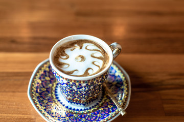 A cup of hot milk  in an antique Thai traditional benjarong style containers, on wood  table, Sensitive focus.