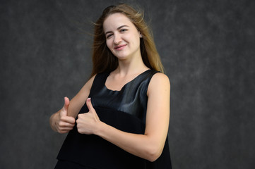 Studio photo portrait of a pretty student girl, brunette young woman with long beautiful hair in a black T-shirt on a gray background. Smiling, talking, showing emotions