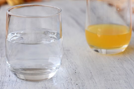 Closeup glass of fresh water and juice at the background/ Conceptual image of half full-half empty glass