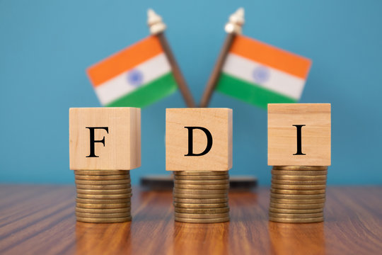 Concept Of FDI Or Foreign Direct Investment On India In Wooden Block Letters On Stack Of Coins With Indian Flag As A Background.