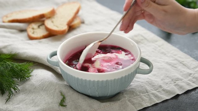Plate of ukrainian and russian national food red beet soup borscht with beef. Female hand take sour cream to a plate