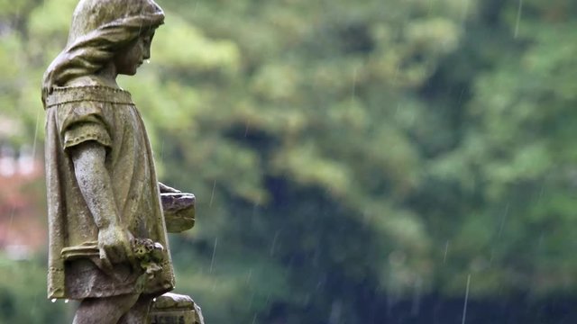 Angel girl stone grave headstone in rainy cemetery. Sad, mourning, sorrow remembrance figure.