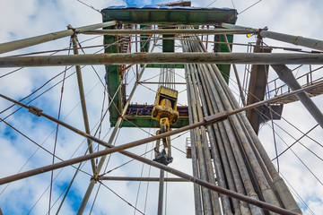 Location of equipment inside the oil and gas drilling rig. Drill pipes stand upright. Lifting system. View from bottom to top. Work is underway to raise drill pipes from the well.