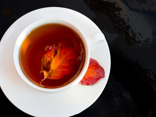 autumn leaf flowing in a white cup of tea on a dark background